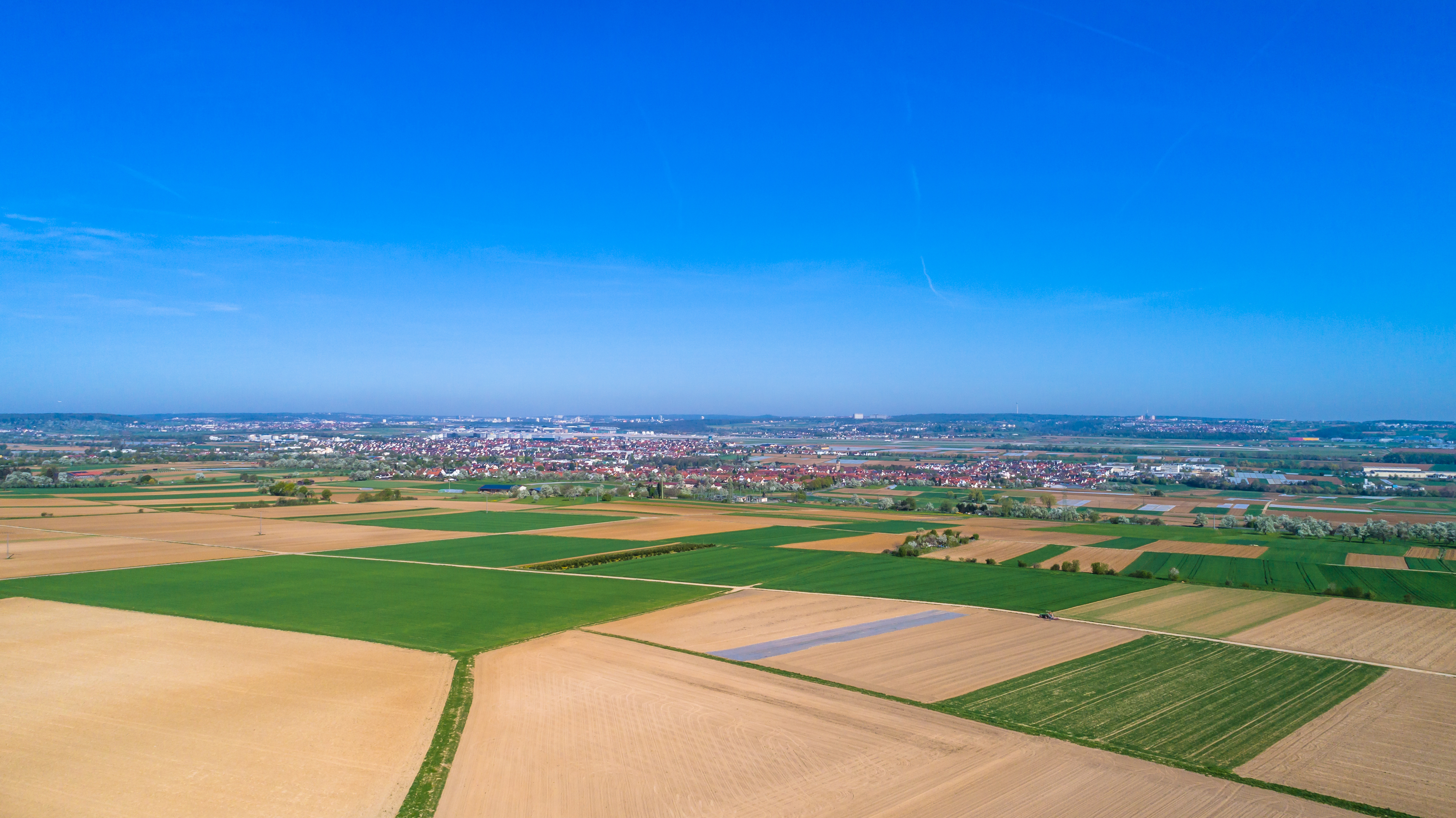 Luftaufnahme von Feldern mit einer Stadt im Hintergrund unter blauem Himmel.