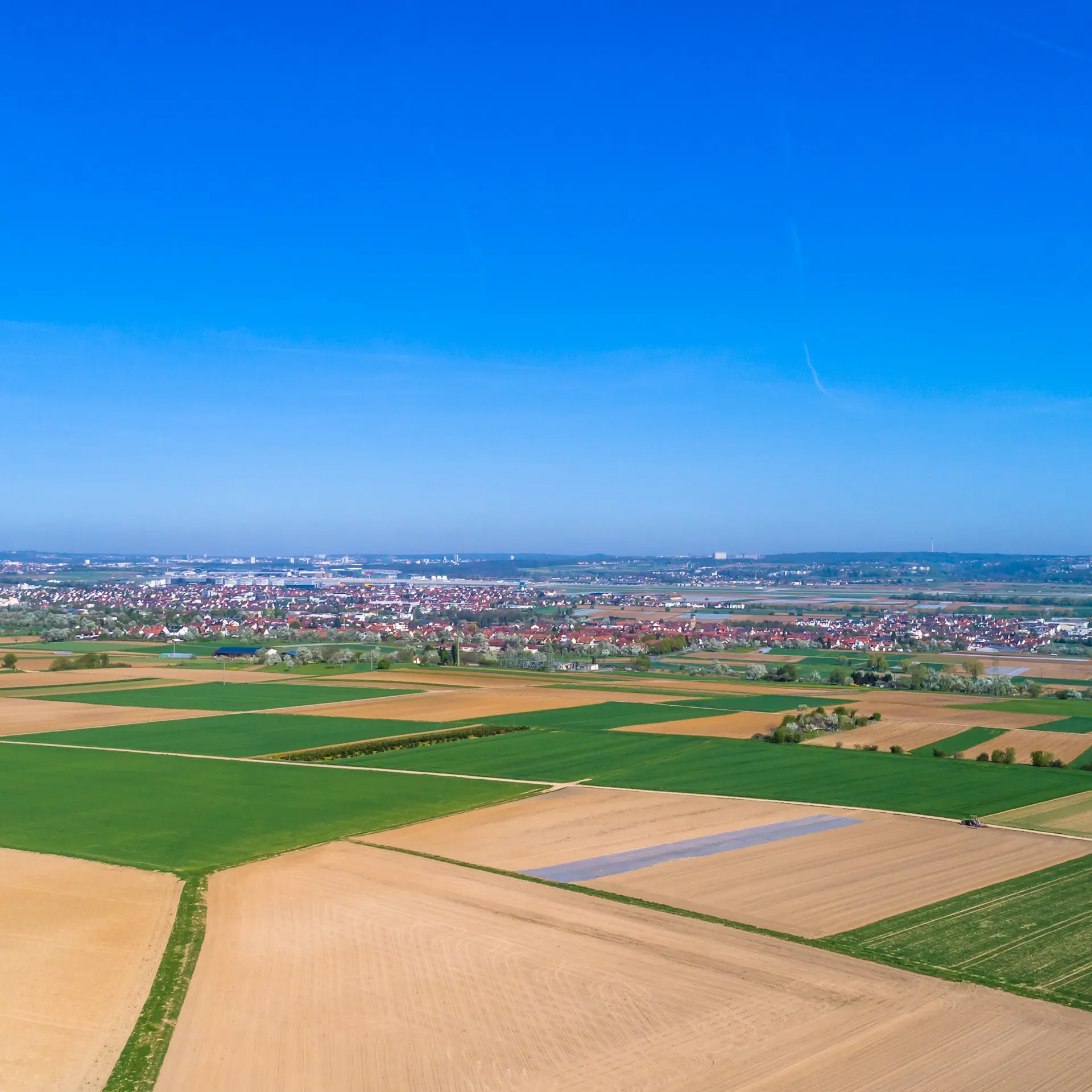 Luftaufnahme von Feldern mit einer Stadt im Hintergrund unter blauem Himmel.