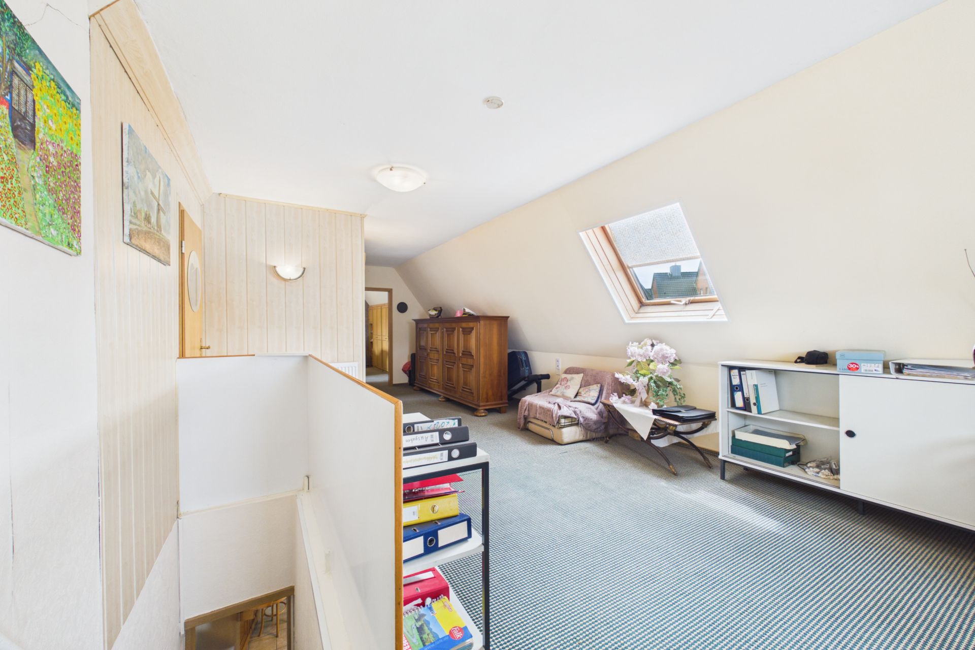 Helles Dachgeschosszimmer mit Sofa, Sessel, Schrank, Regal und Dachfenster.