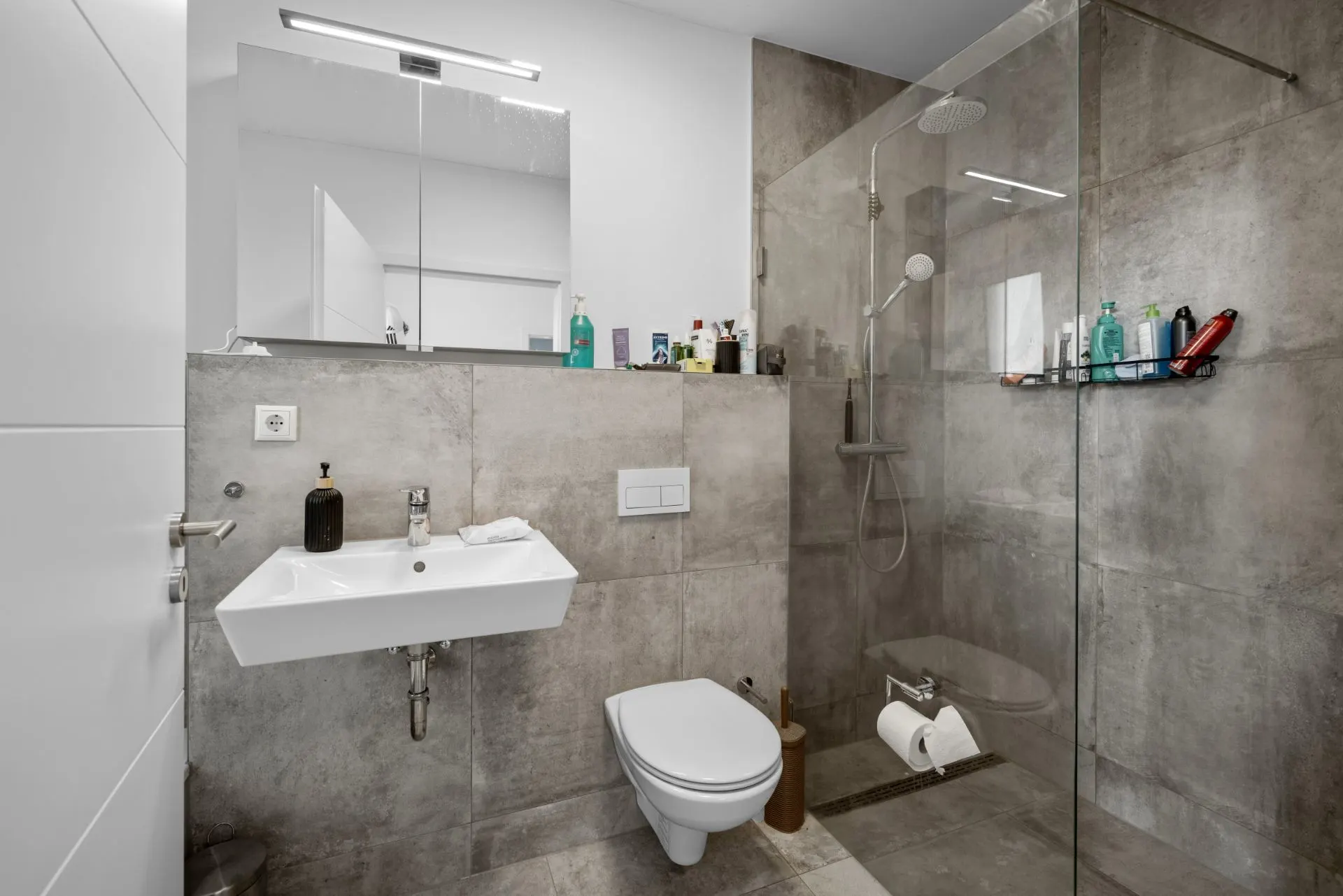 Modernes Badezimmer mit Waschbecken, Toilette und ebenerdiger Dusche mit Glaswand.