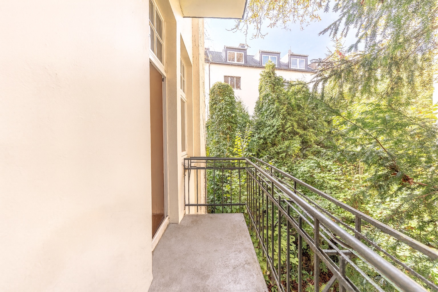 Kleiner Balkon mit Metallgeländer und Blick auf grüne Bäume und Nachbargebäude.