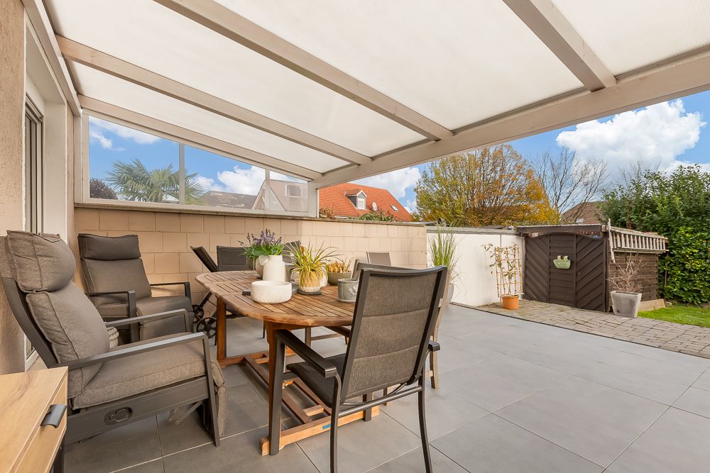 Überdachte Terrasse mit Tisch, Stühlen und Pflanzen, Blick auf Garten und Geräteschuppen.