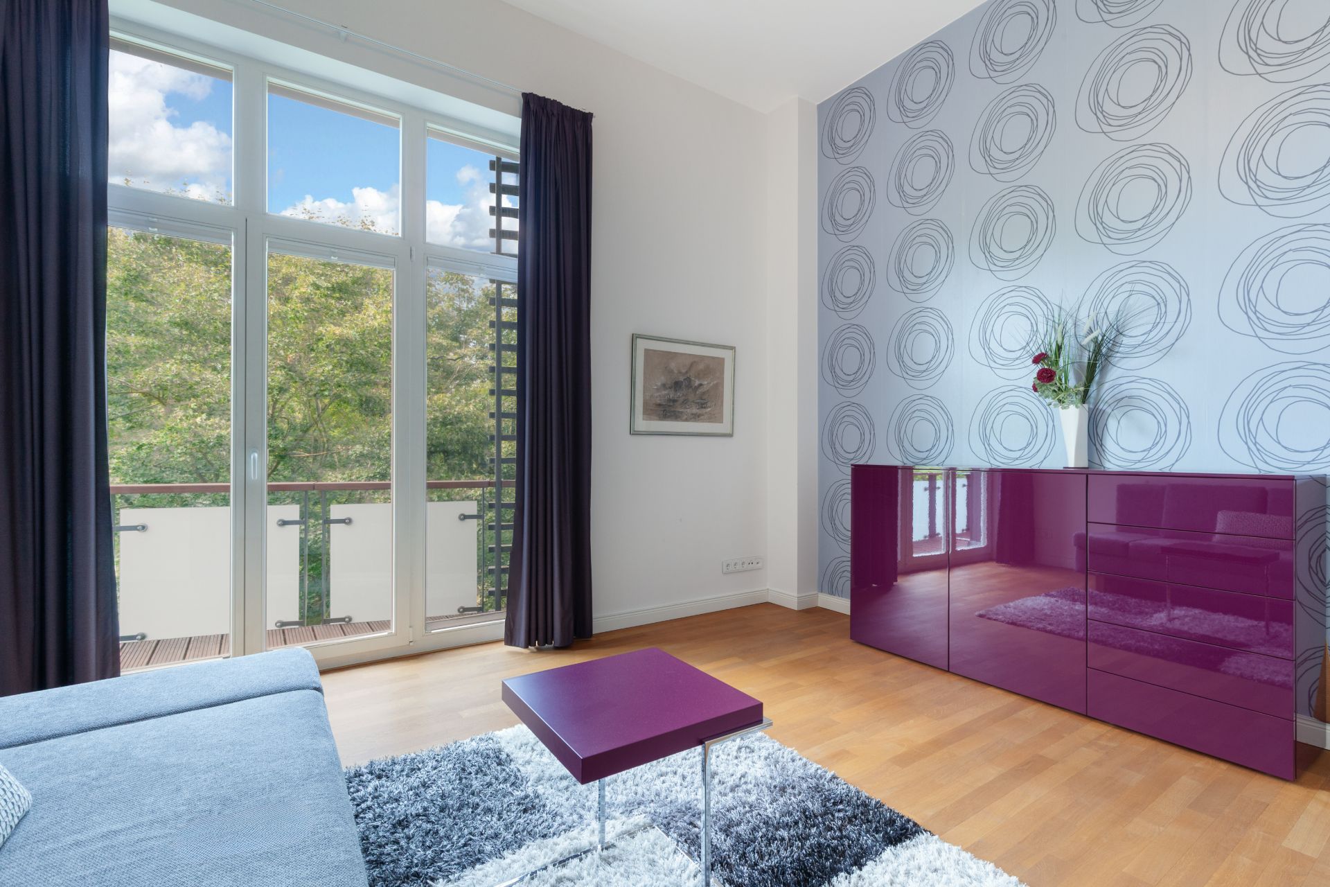 Modernes Wohnzimmer mit lila Möbeln, großem Fenster und gemusterter Akzentwand.