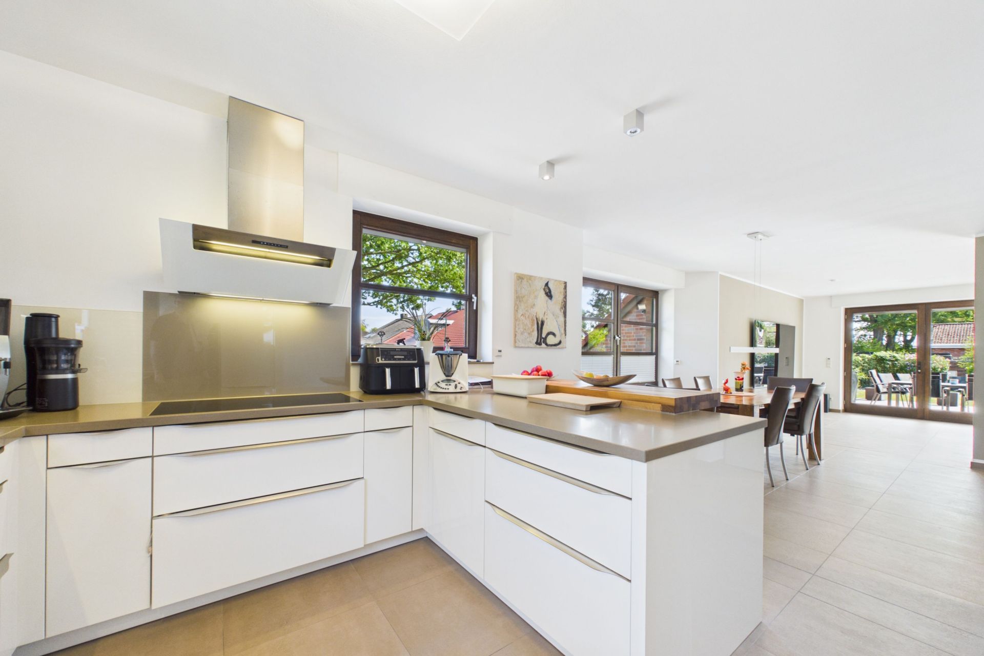 Moderne, helle Küche mit weißen Schränken und Essbereich im Hintergrund.