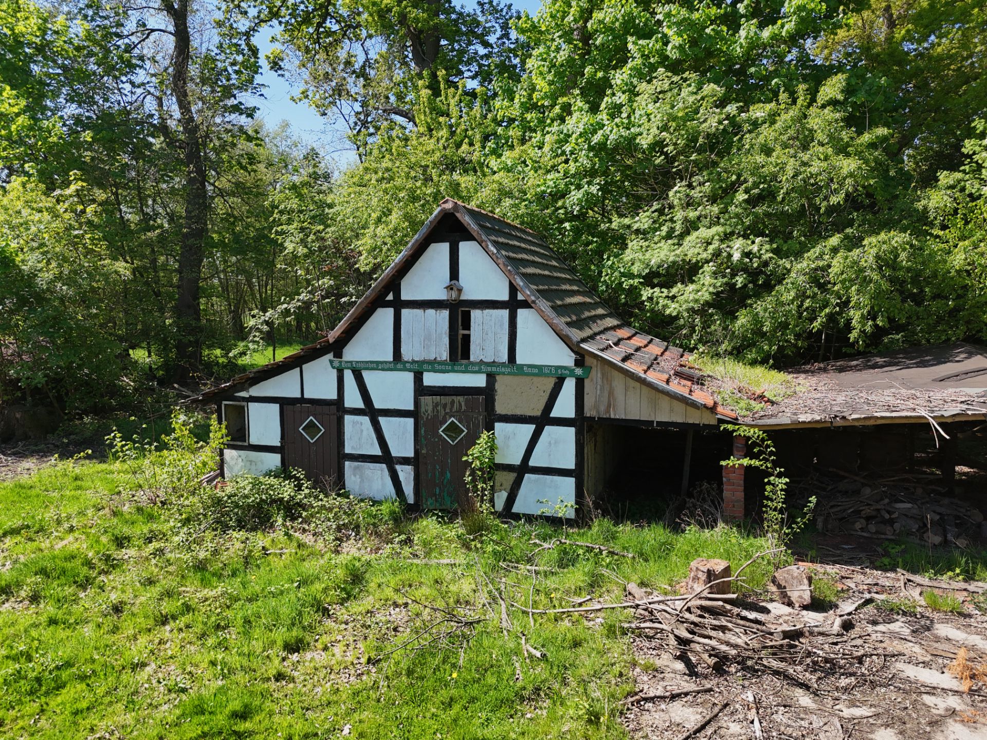 Altes Fachwerkhaus mit schrägem Dach, umgeben von Bäumen und Gras.