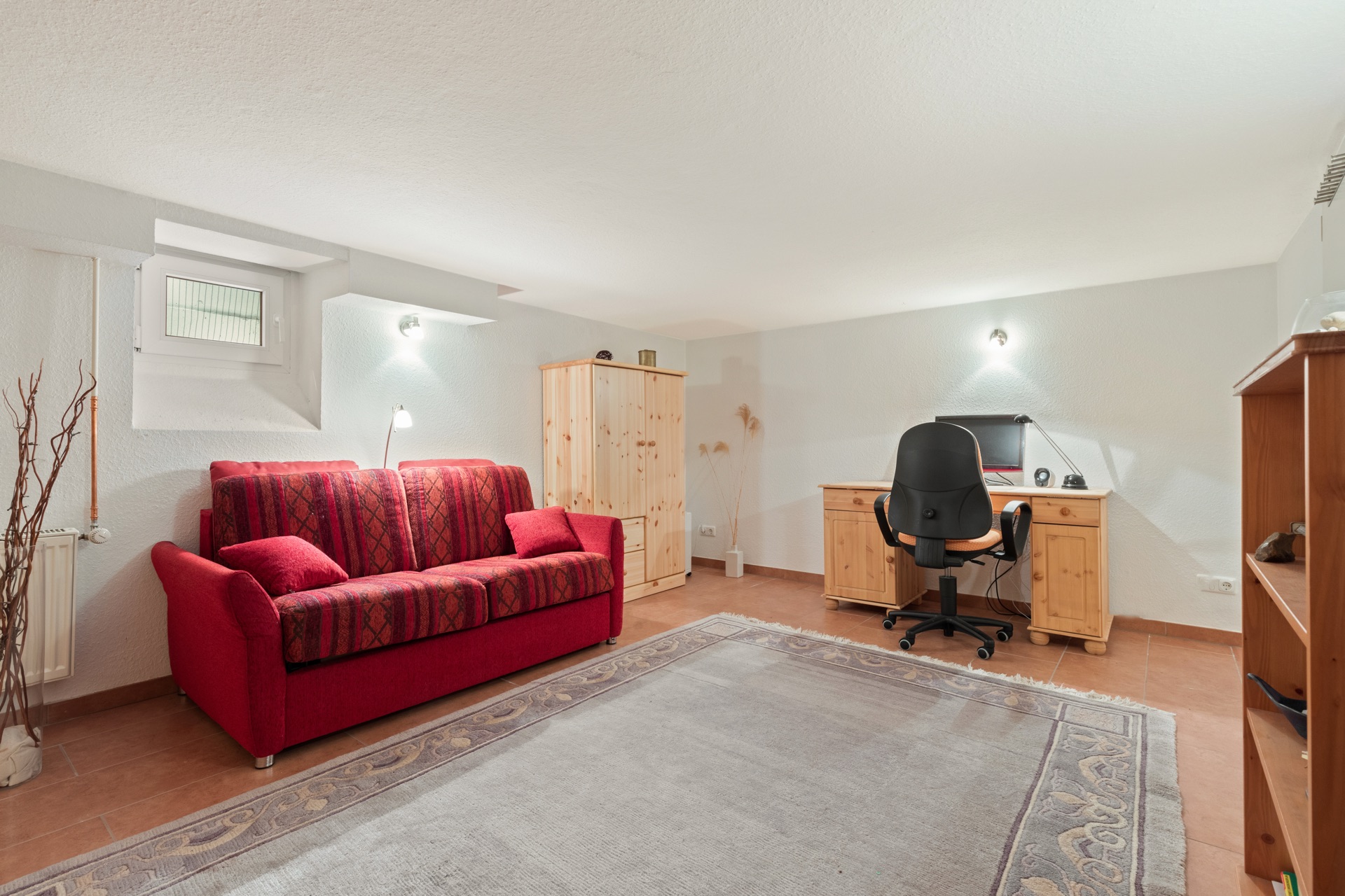 Wohnraum mit rotem Sofa, Holzmöbeln, Teppich und Schreibtisch mit Stuhl.