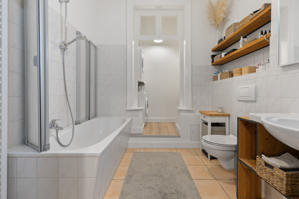 Modernes Badezimmer mit Badewanne, WC, Waschbecken und Regalen, im Hintergrund Waschmaschine.