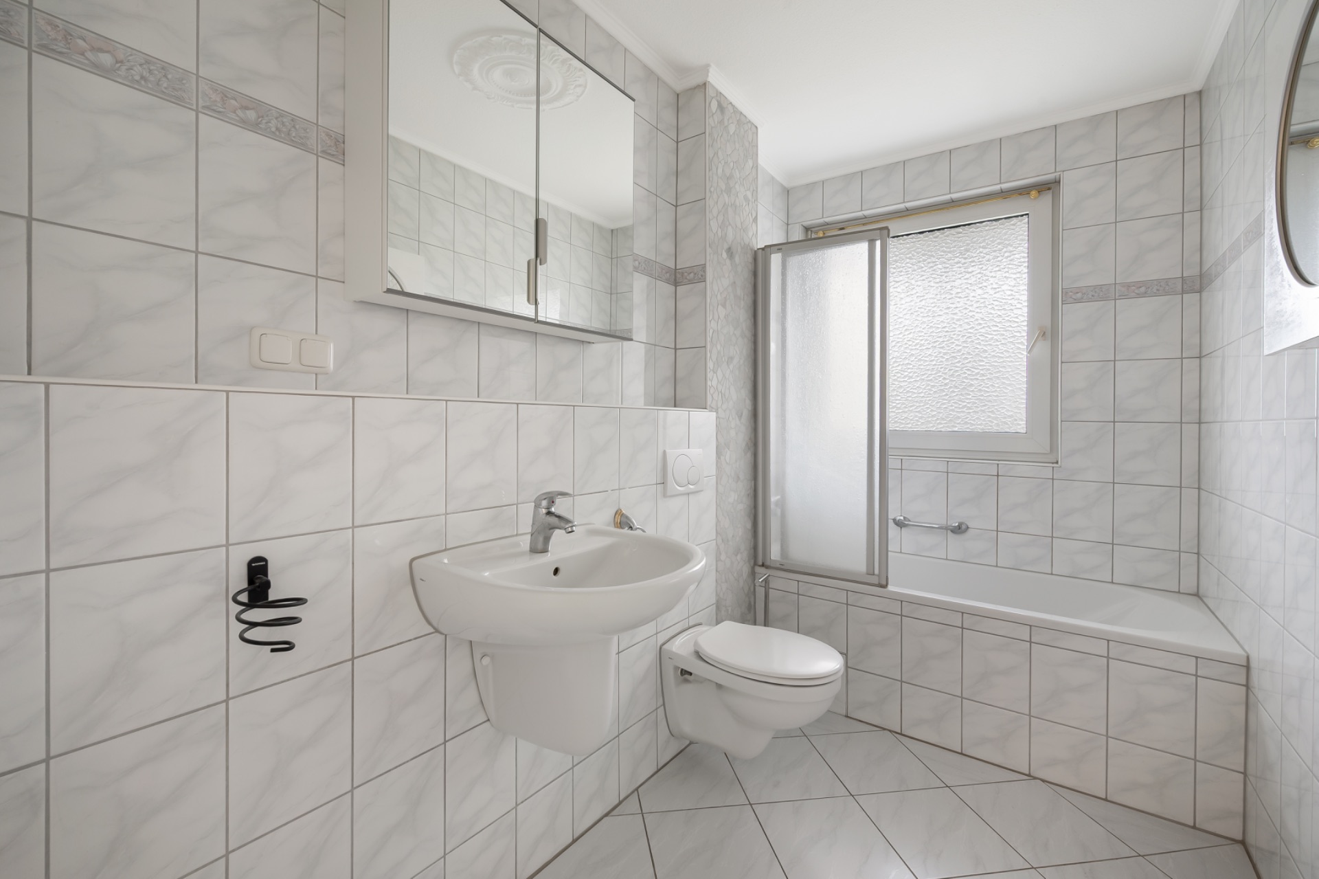 Helles Badezimmer mit Waschbecken, WC, Badewanne und Spiegelschrank.