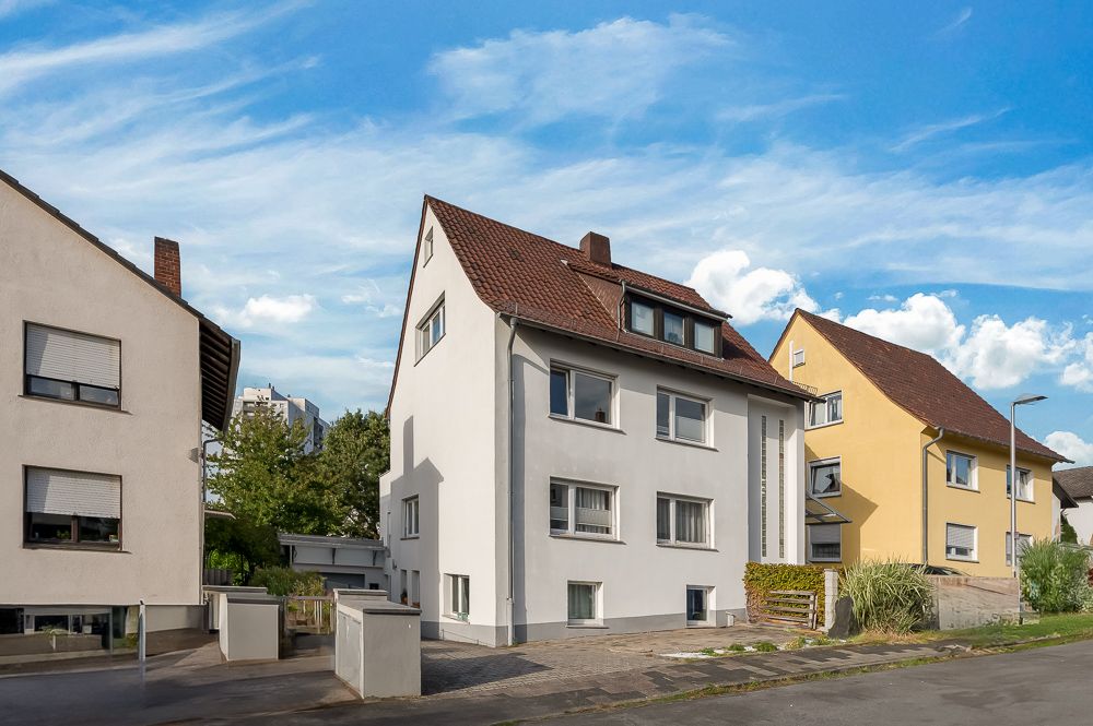 Dreistöckiges Wohnhaus mit Satteldach und hellgrauer Fassade an einer Wohnstraße.