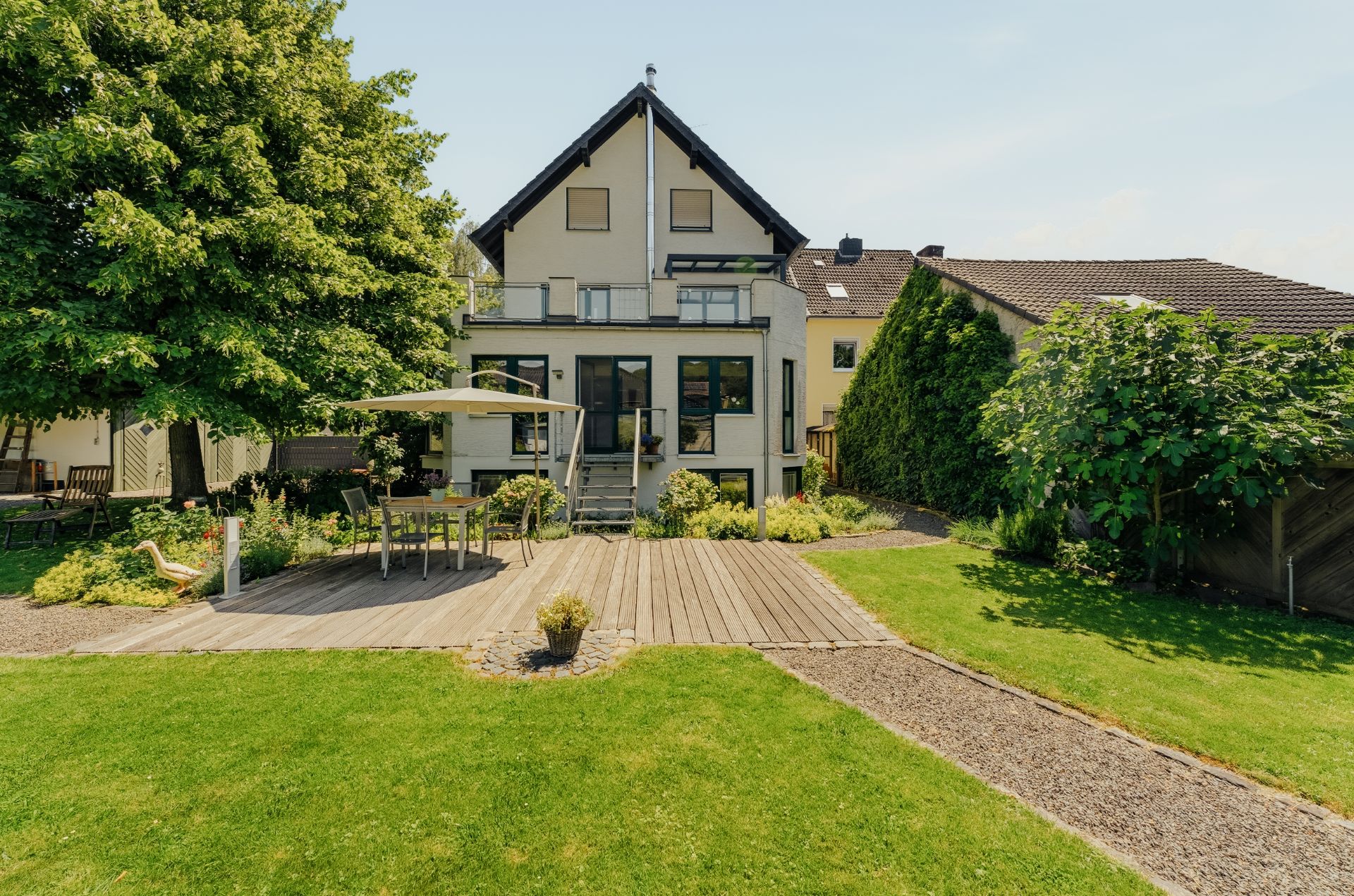 Gepflegter Garten mit Terrasse, Esstisch und Stühlen vor einem Wohnhaus mit Satteldach.