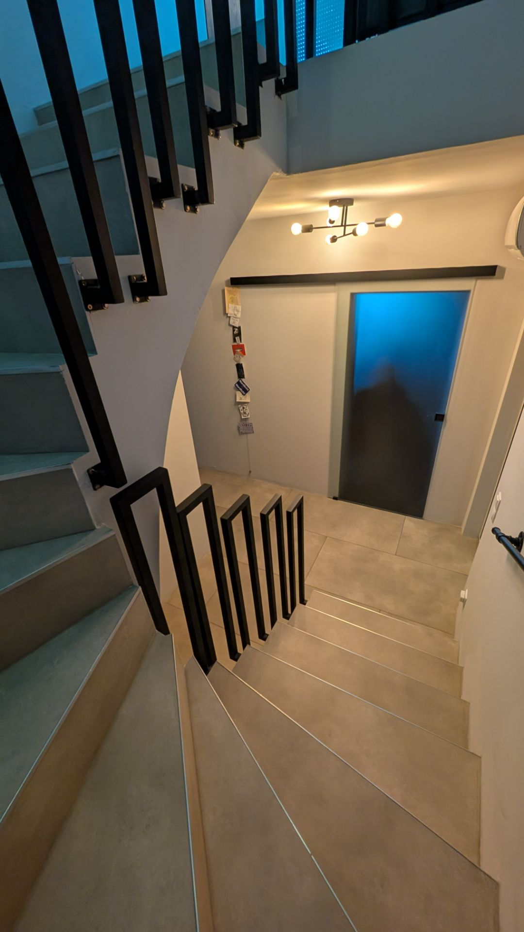 Moderne Treppe mit schwarzen Geländern, Fliesenboden und beleuchtetem Flur mit geschlossener Tür.