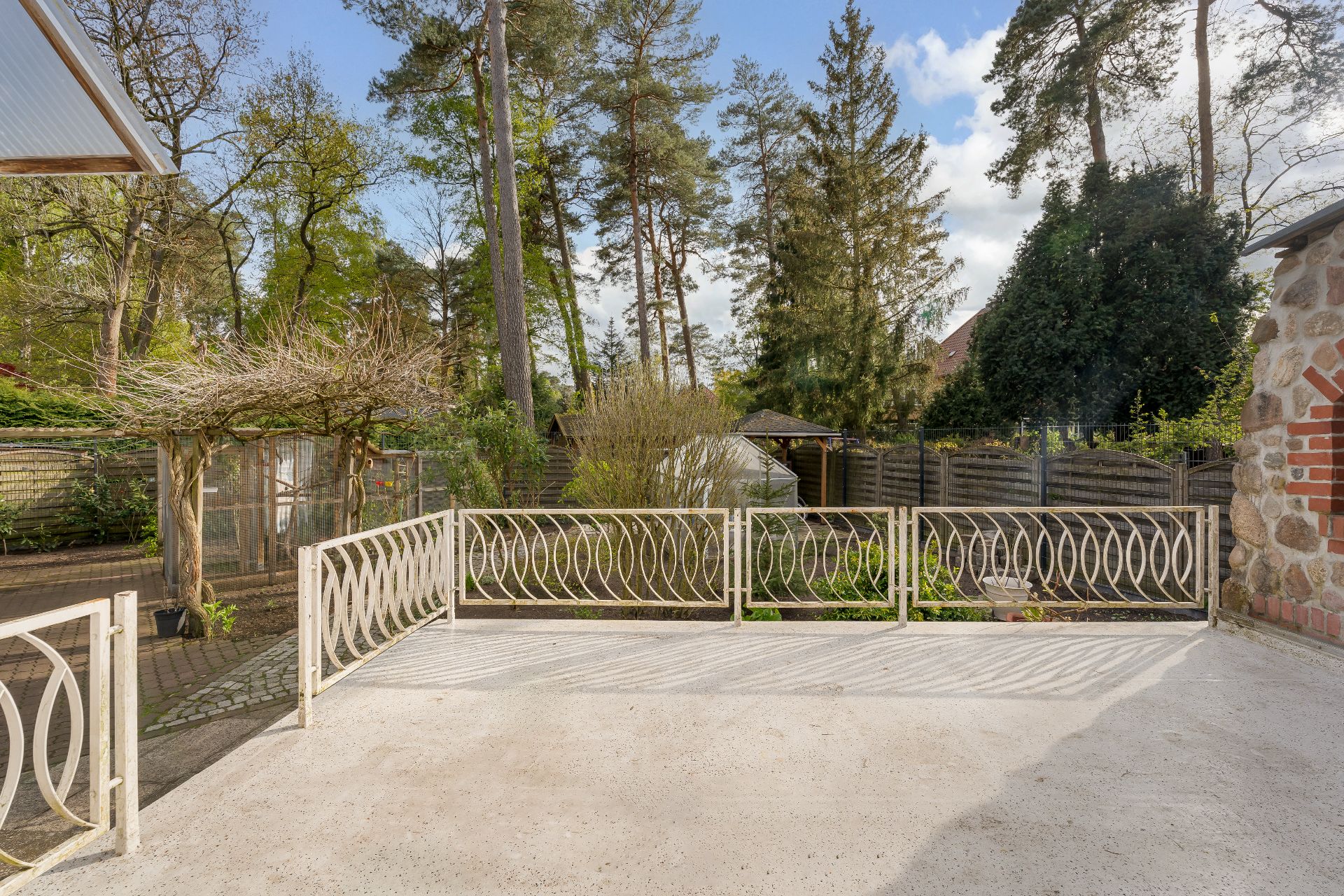 Terrasse mit hellem Geländer und Blick auf Garten mit Bäumen und Holzzaun.
