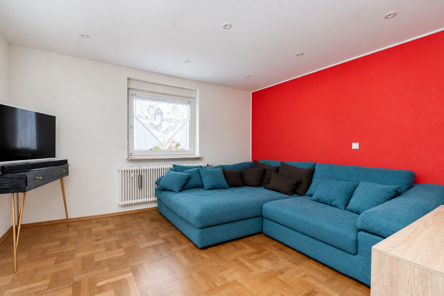 Wohnzimmer mit blauer Eckcouch, roter Wand und Fernseher auf kleinem Tisch.