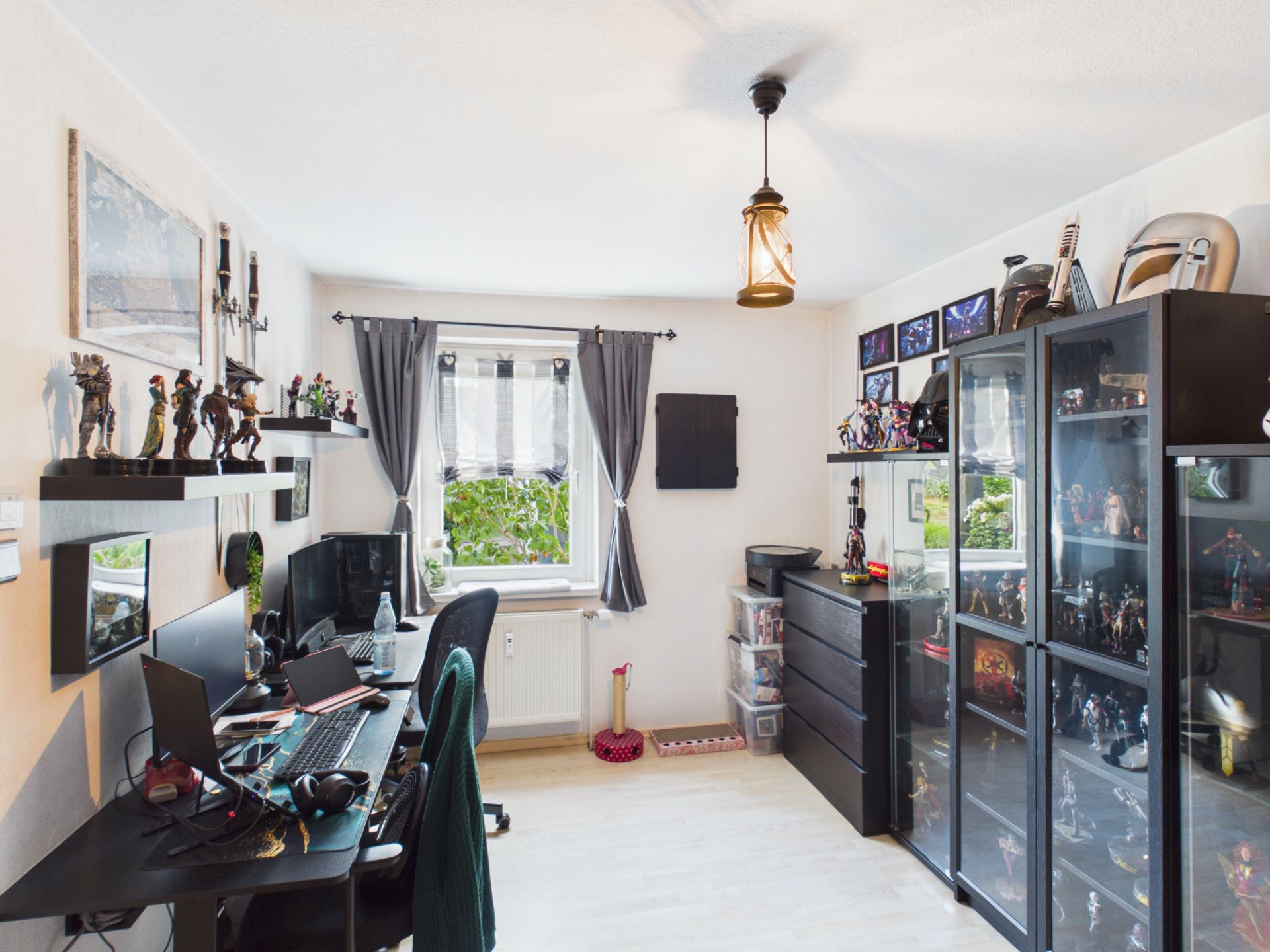 Helles Arbeitszimmer mit Schreibtisch, Computern, Glasvitrinen und Sammlerfiguren.