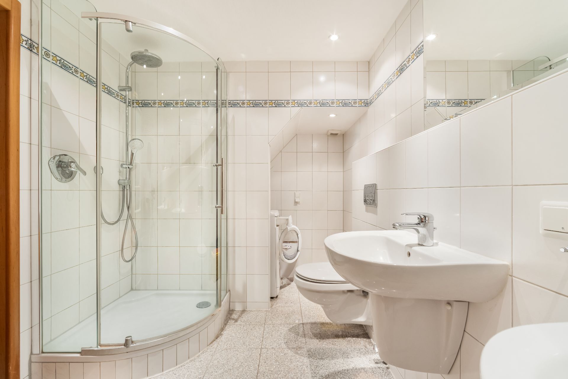 Helles Badezimmer mit Dusche, WC und Waschbecken, gefliest und mit Spiegel.