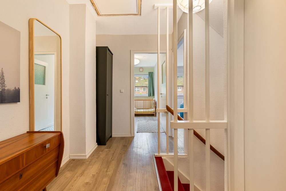 Heller Flur mit Spiegel, Holzkommode und Zugang zu weiteren Zimmern, Treppe rechts.