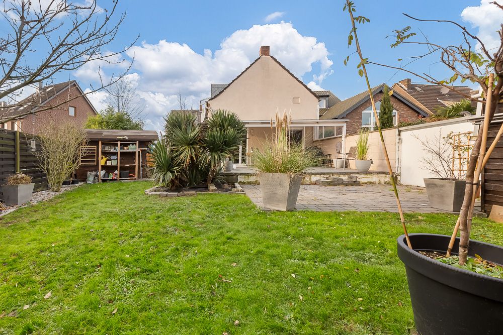Grüner Garten mit Rasen, Pflanzkübeln, Terrasse und Schuppen, Einfamilienhaus im Hintergrund.