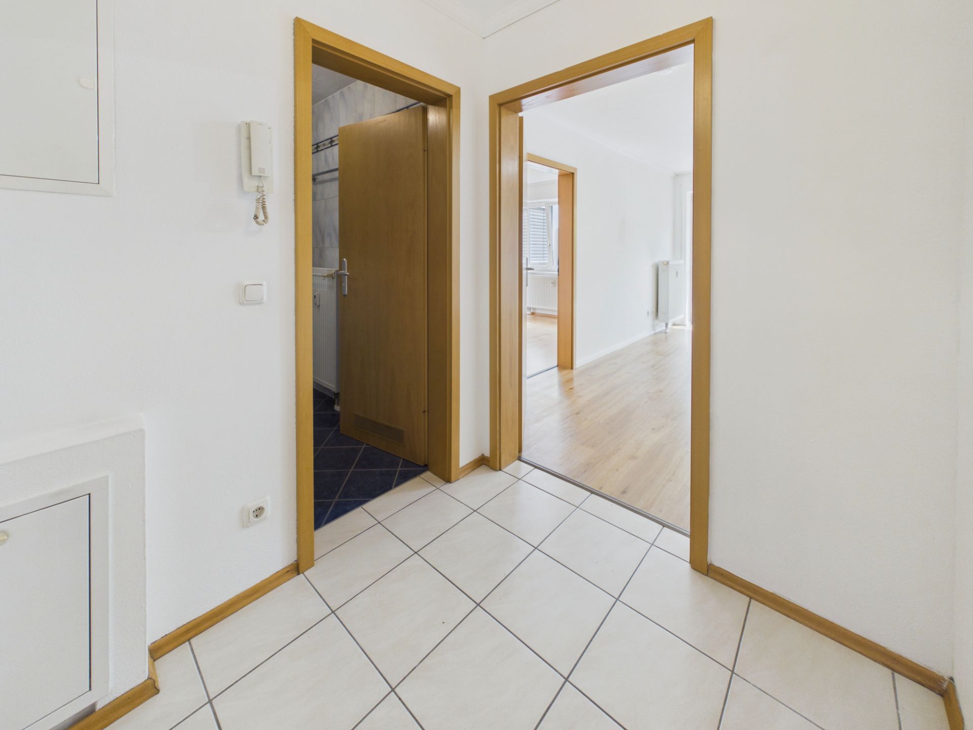 Flur mit Fliesenboden und zwei offenen Türen, die in verschiedene Zimmer führen.