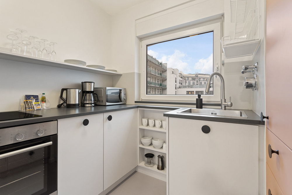 Moderne, helle Küche mit Herd, Backofen, Spüle und großem Fenster mit Stadtblick.