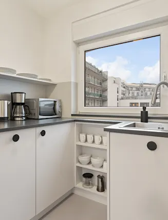 Moderne, helle Küche mit Herd, Backofen, Spüle und großem Fenster mit Stadtblick.