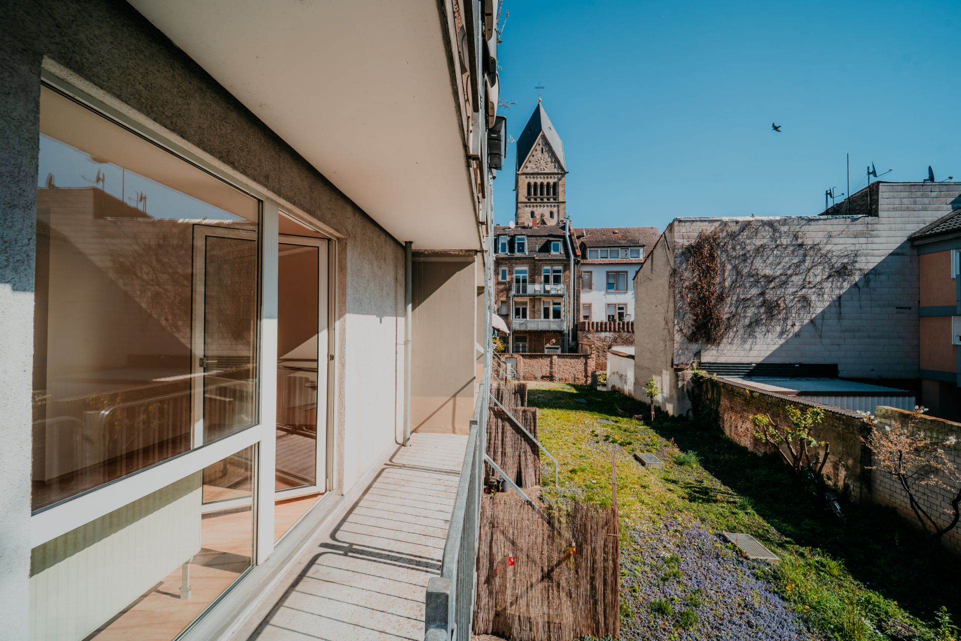 Balkon mit Blick auf einen begrünten Hinterhof und benachbarte Gebäude bei sonnigem Wetter.