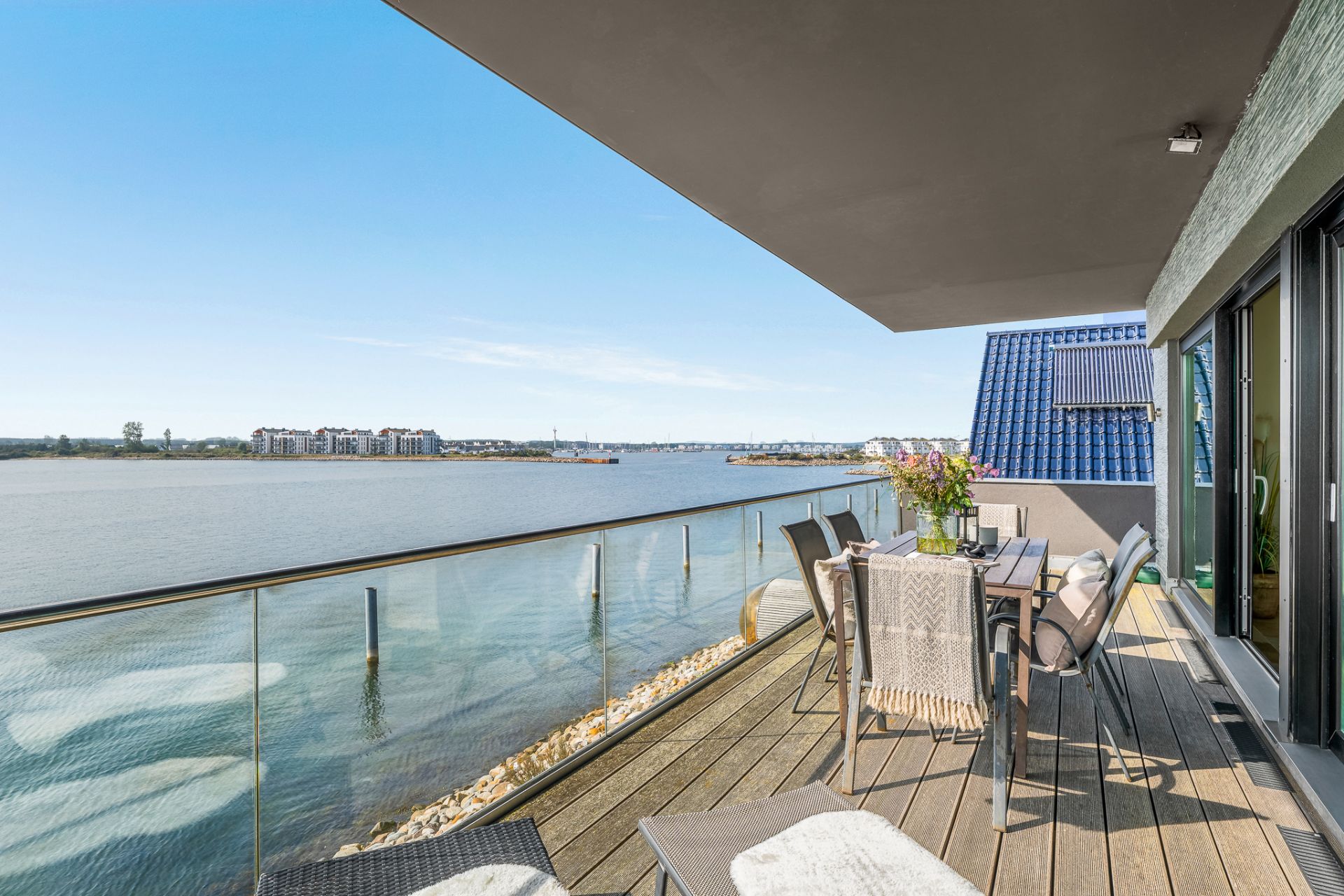 Großer Balkon mit Glasgeländer, Esstisch und Blick auf einen Fluss oder See.