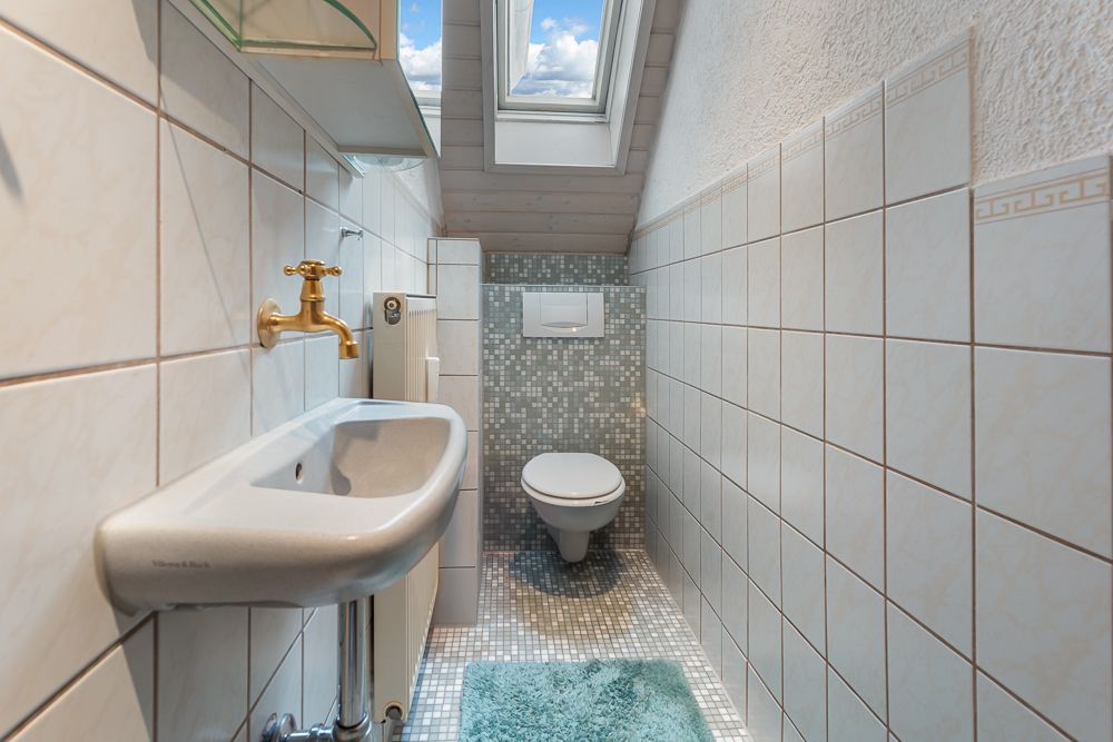 Kleines Badezimmer mit Wandwaschbecken, Toilette, Dachfenster und türkisfarbenem Teppich.