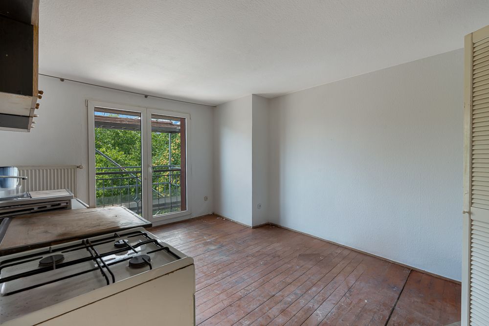 Leerer Raum mit Holzboden, Gasherd und Doppeltür mit Blick auf einen Balkon.