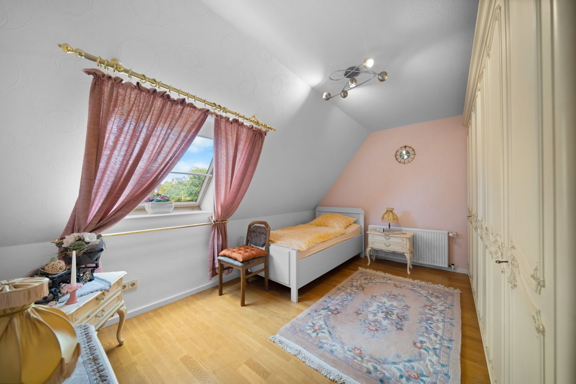 Kleines Schlafzimmer mit Einzelbett, rosa Vorhängen, Teppich und großem Kleiderschrank.