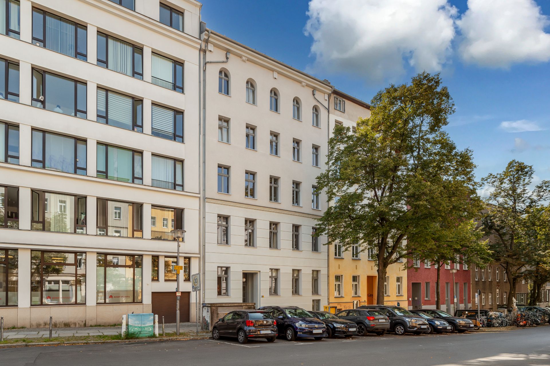 Mehrstöckiges Wohngebäude mit parkenden Autos und Bäumen an der Straße.