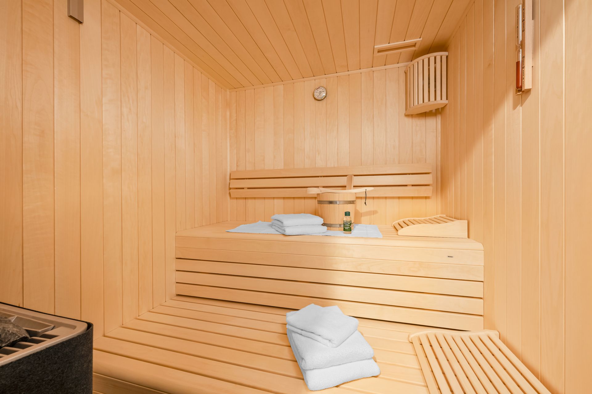 Helle Holzsauna mit Handtüchern, Saunaofen und Eimer auf der Bank.