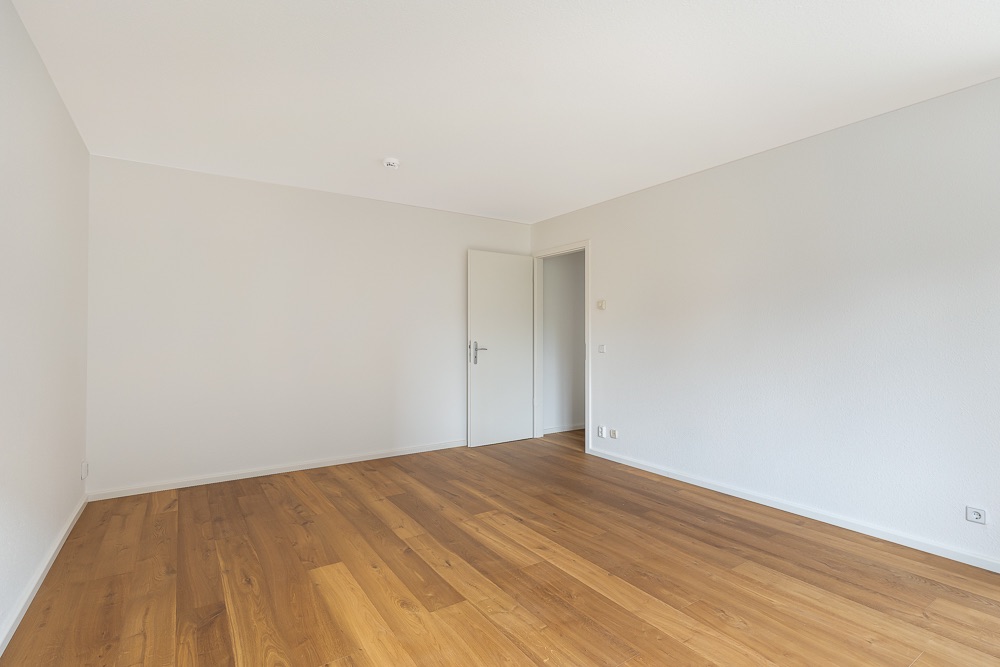 Leerer Raum mit Holzfußboden, weißen Wänden und einer offenen Tür.