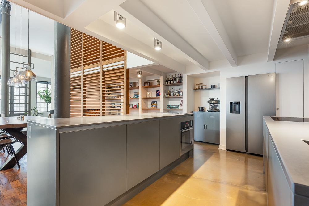 Moderne Küche mit grauen Schränken, großer Kochinsel und offenem Regal neben einem Kühlschrank.
