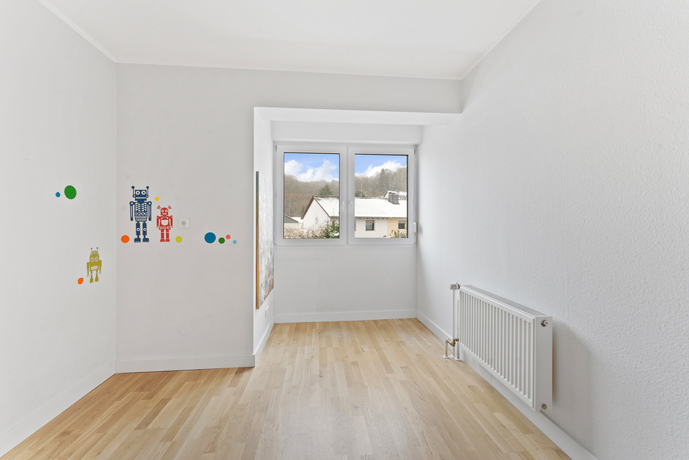 Helles Kinderzimmer mit Holzboden, Wandstickern von Robotern und großem Fenster.