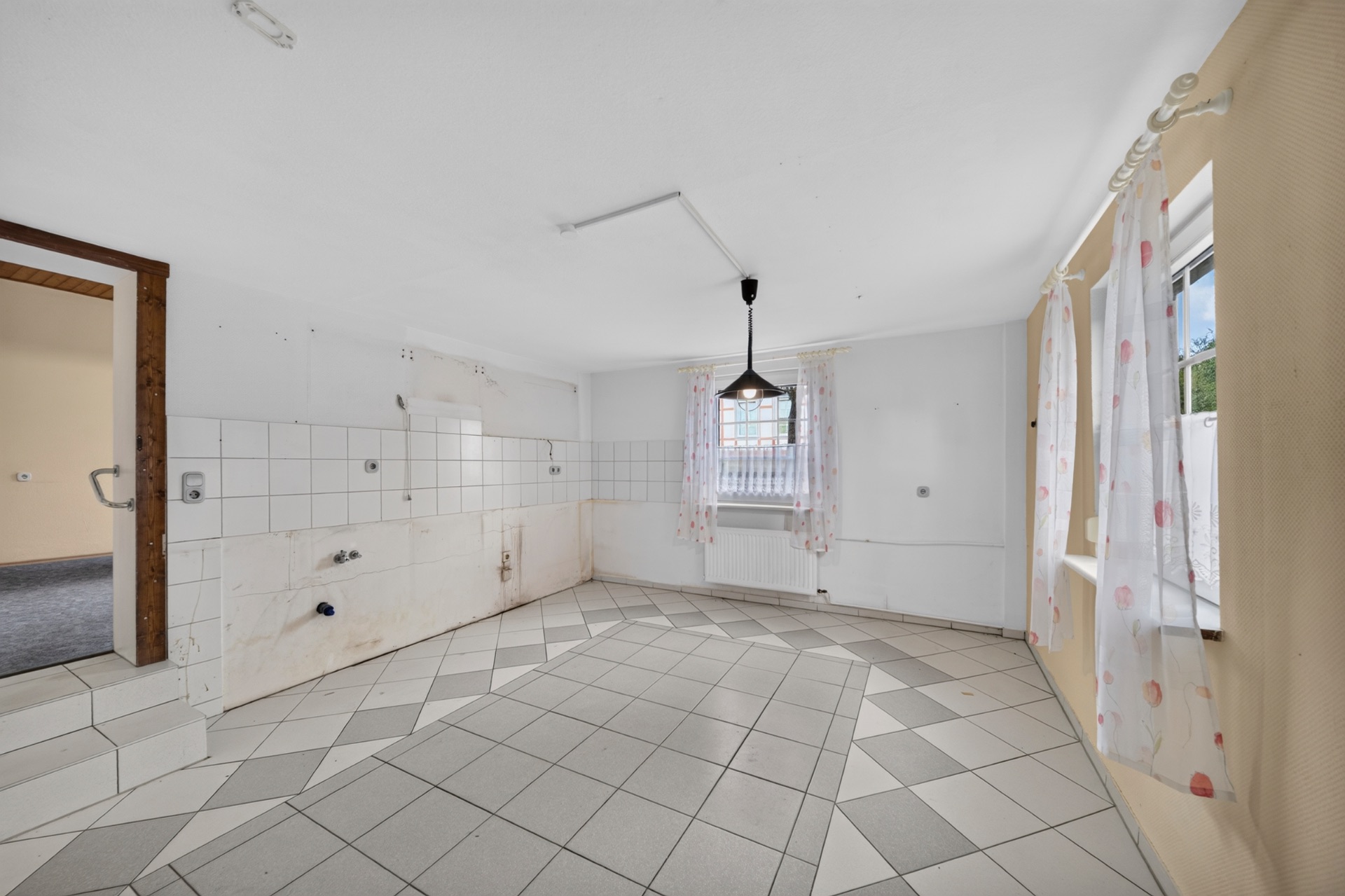 Leerer, gefliester Raum mit zwei Fenstern, weißen Wänden und einer Deckenlampe.
