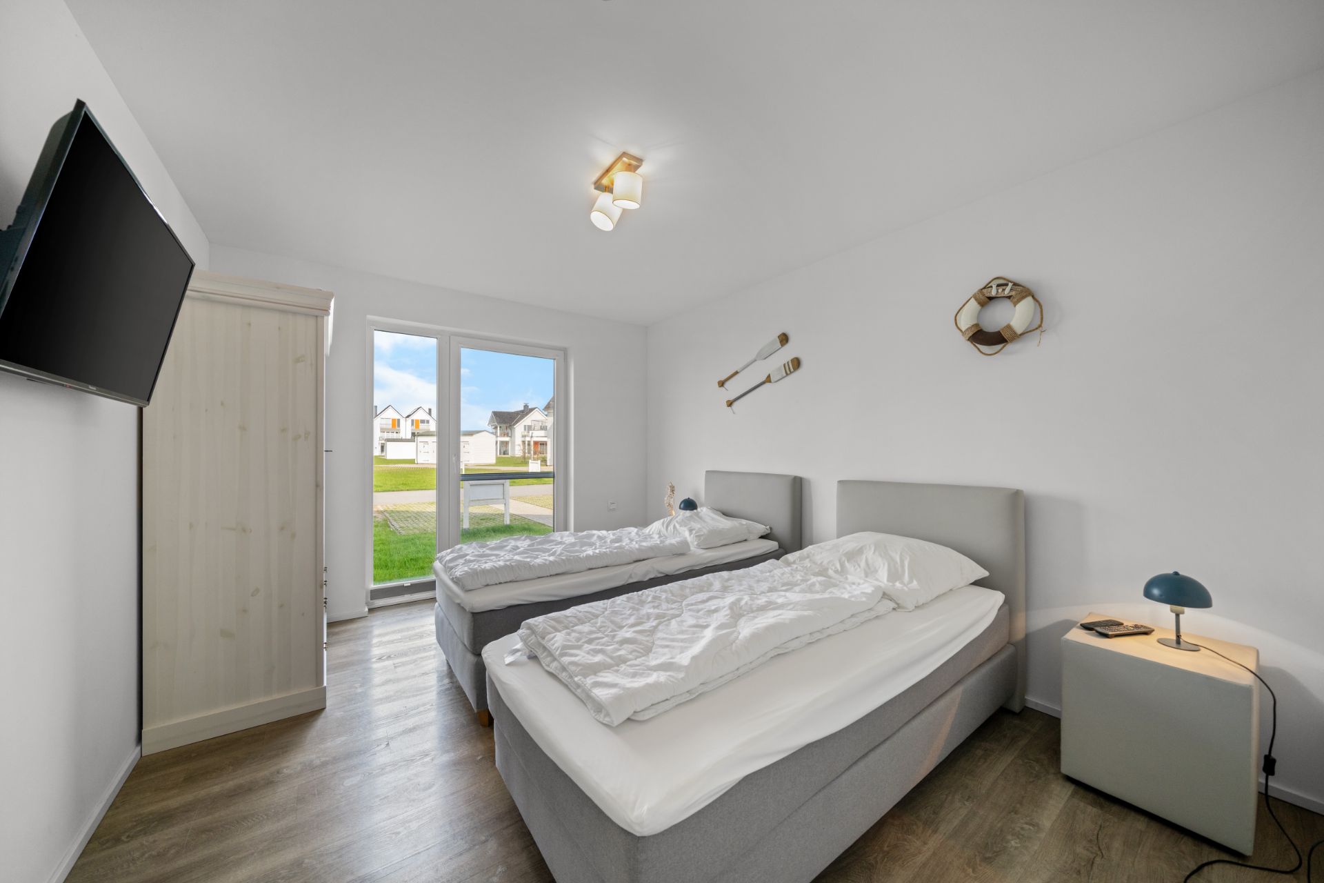 Zweibettzimmer mit zwei Einzelbetten, Schrank, TV, Nachttisch und Dekoration an der Wand.