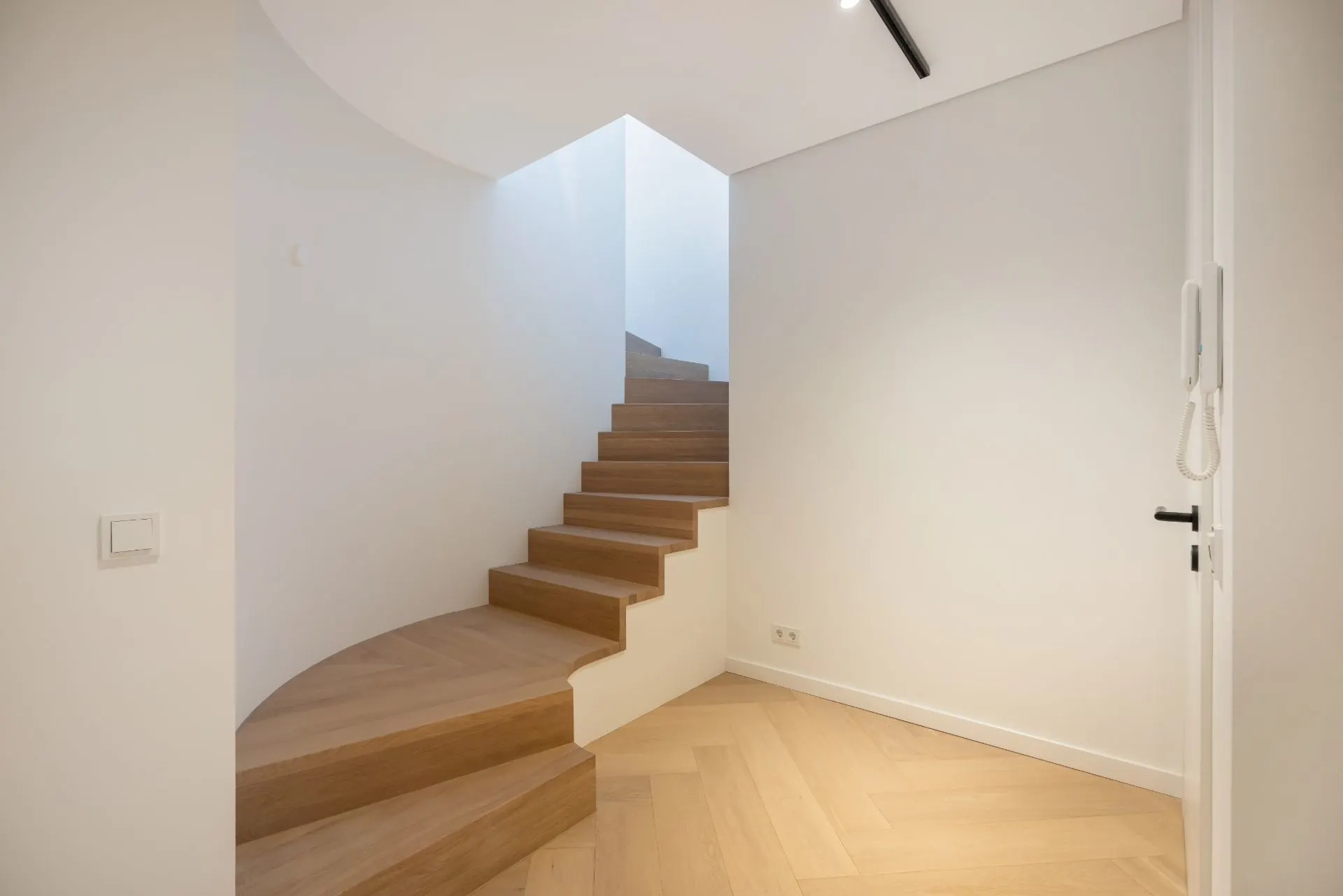 Helle Diele mit moderner Holztreppe und weißen Wänden.