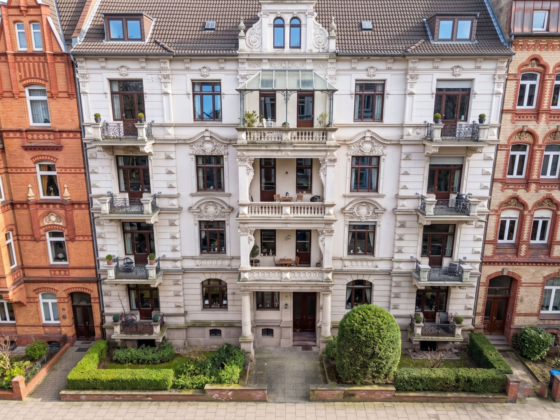 Fünfstöckiges Wohnhaus mit Balkonen und verzierten Fassadendetails, umgeben von Vorgärten.