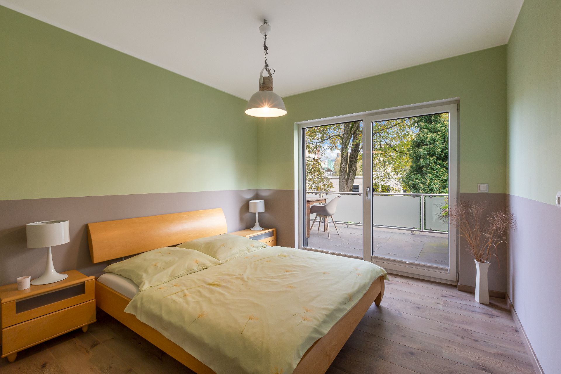 Schlafzimmer mit Doppelbett, Nachttischen und Zugang zu einem Balkon mit Sitzgelegenheit.