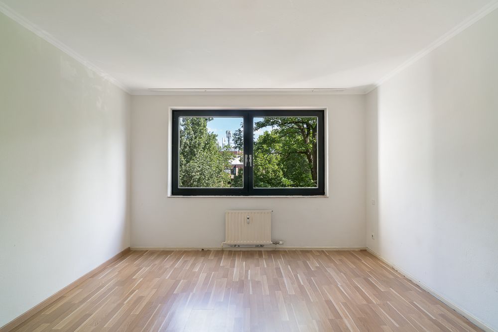 Leerer Raum mit Holzfußboden, großem Fenster und Blick ins Grüne.