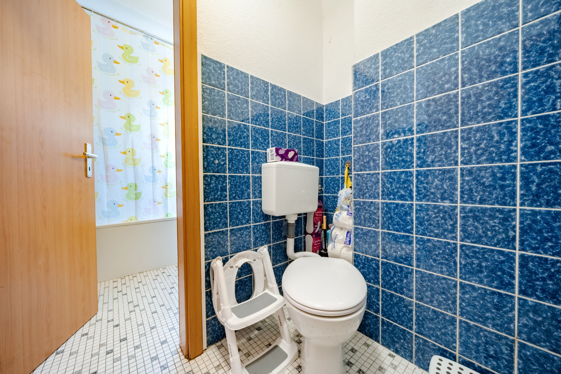 Toilette mit blau gefliesten Wänden, Kindersitz und Utensilien im Badezimmer.