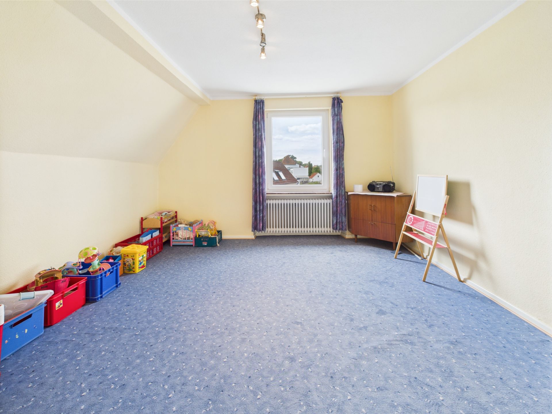 Helles Zimmer mit blauem Teppich, Spielzeugkisten, Fenster, Kommode und Staffelei.