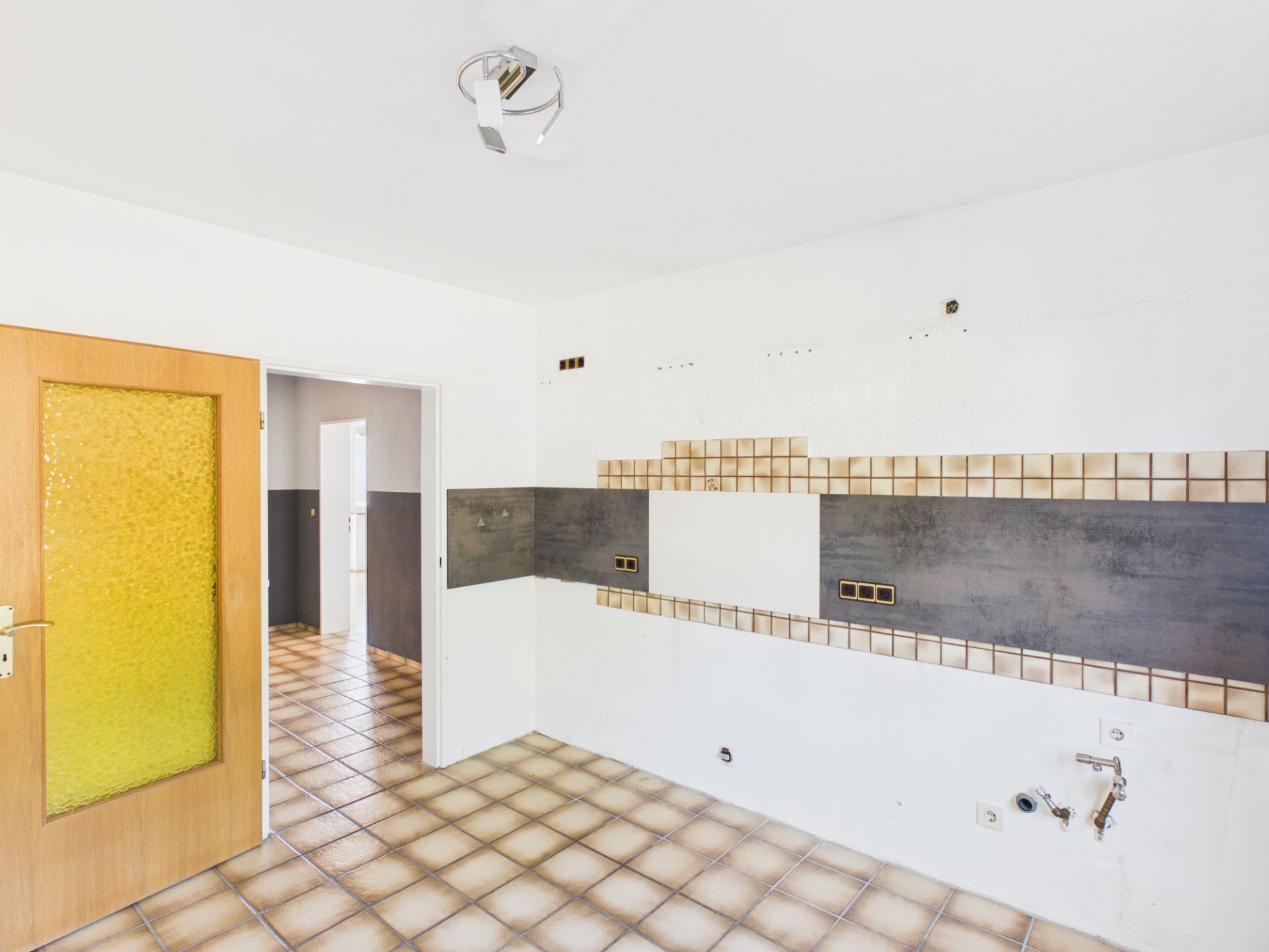 Leerer Raum mit Fliesenboden, gefliester Wand und Tür mit gelbem Glas.