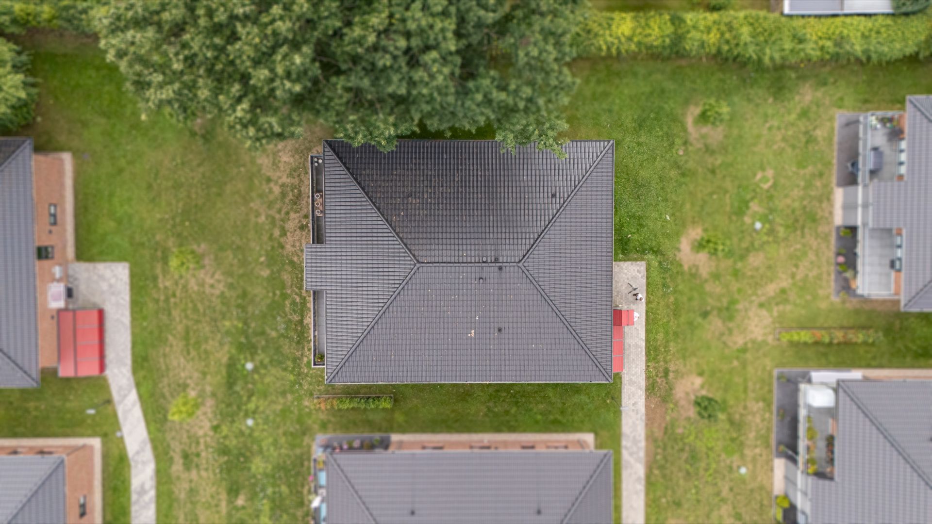 Draufsicht auf ein Wohnhaus mit dunklem Dach und umliegendem Garten.