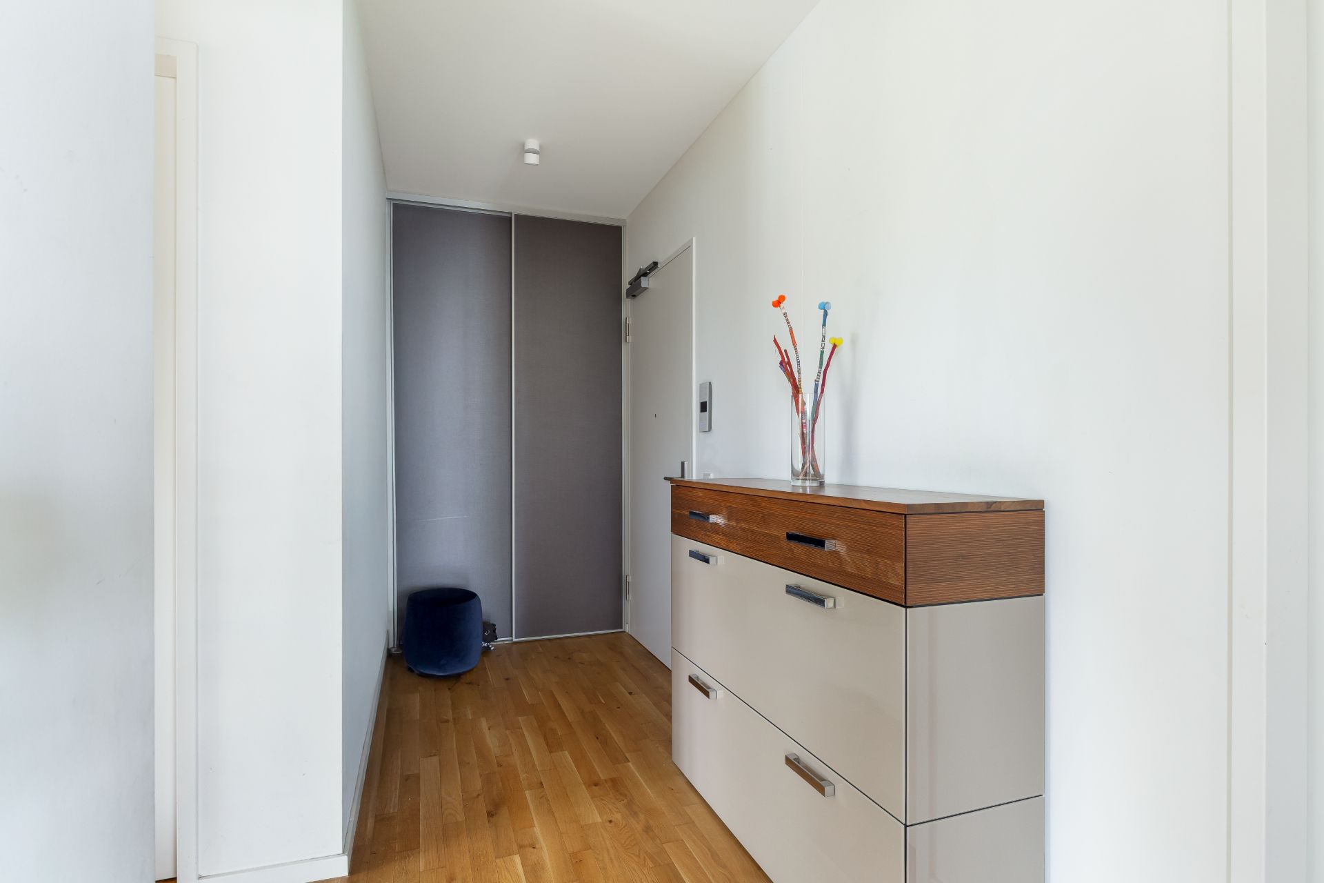 Moderner Flur mit Holzboden, Kommode und Dekovase mit Blumen.