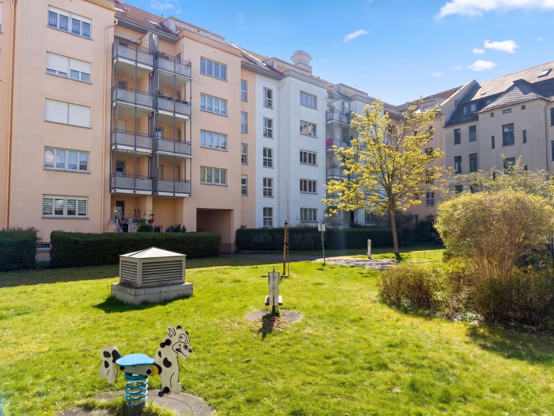 Grüne Wohnanlage mit Spielplatz, Bäumen und Mehrfamilienhäusern im Hintergrund.