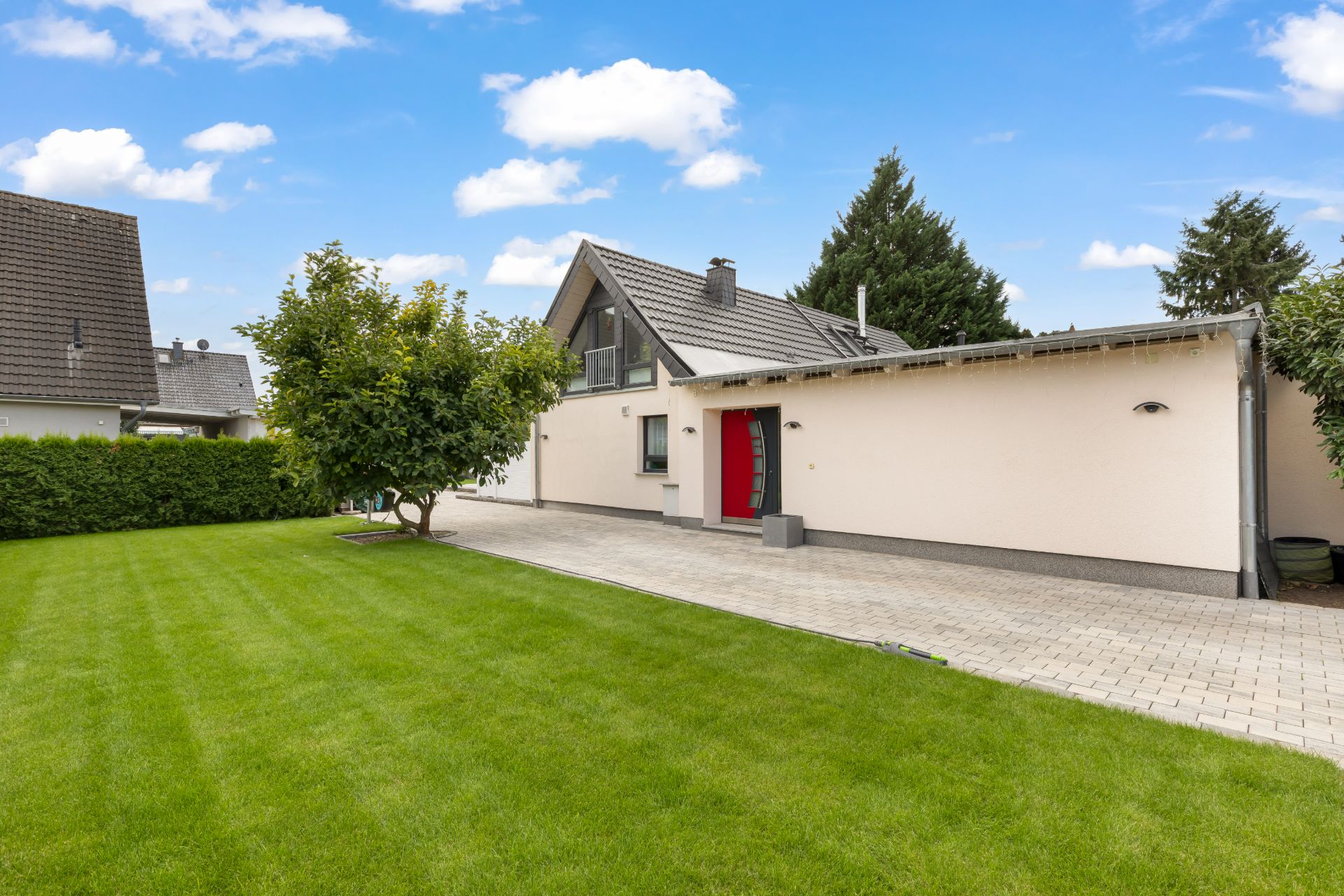 Ein Einfamilienhaus mit roter Tür, gepflastertem Weg und gepflegtem Rasen im Vorgarten.