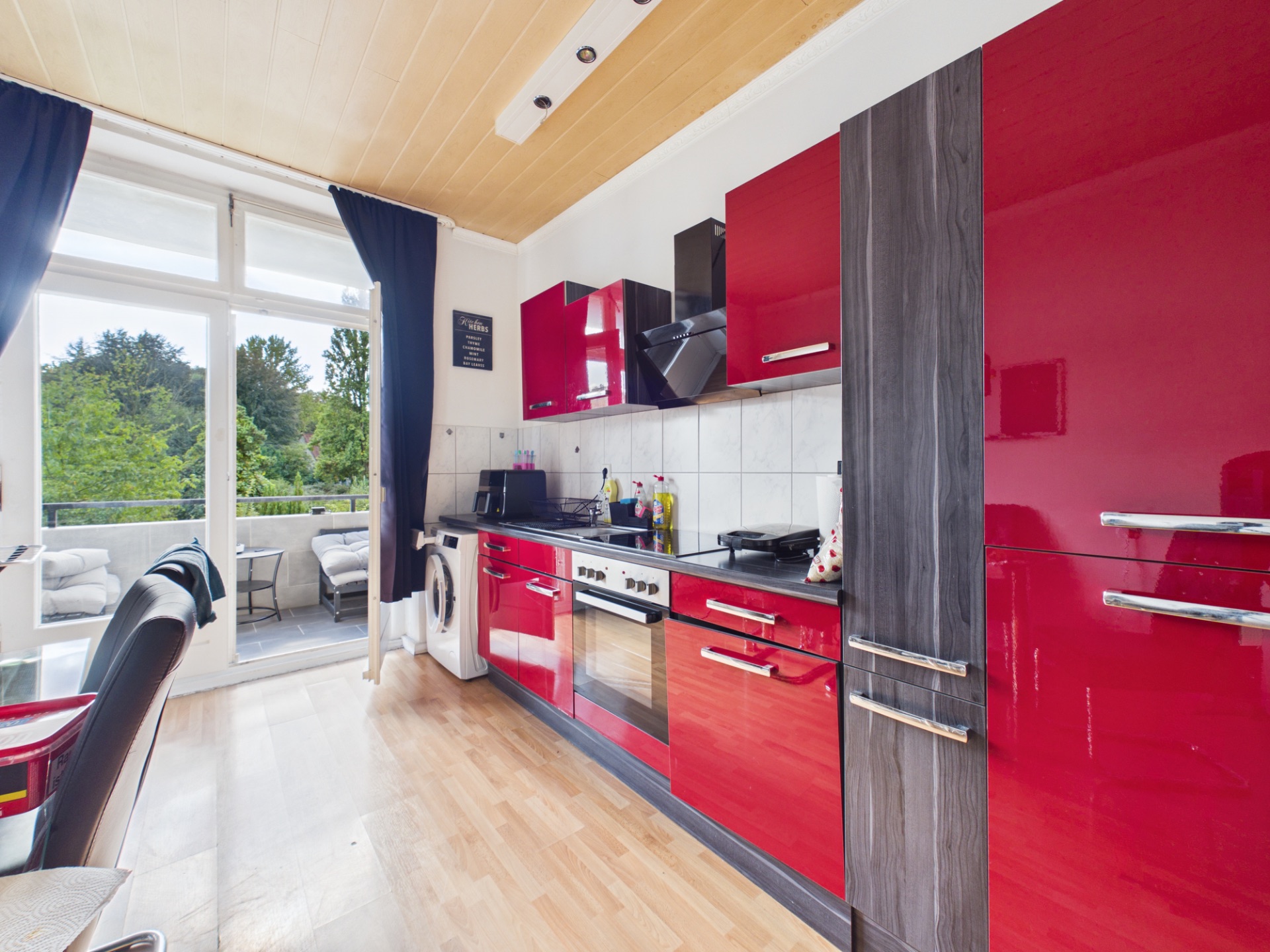 Moderne Küche mit roten Hochglanzfronten und Zugang zu einem Balkon mit Sitzmöbeln.