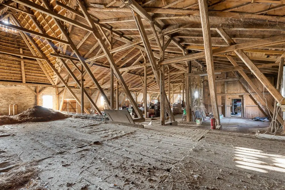 Großer Dachboden mit Holzbalken, offenem Gebälk und einigen gelagerten Gegenständen.