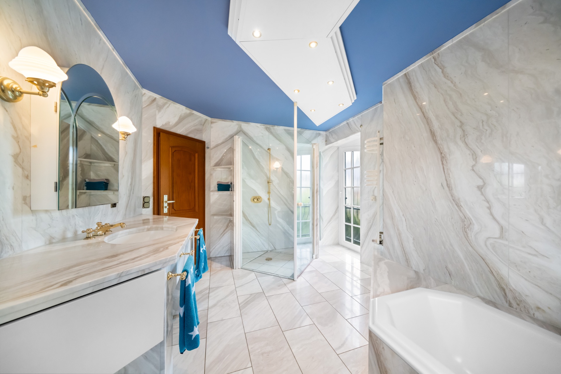 Modernes Badezimmer mit Marmorfliesen, Badewanne, Dusche, Waschtisch und blauem Handtuch.